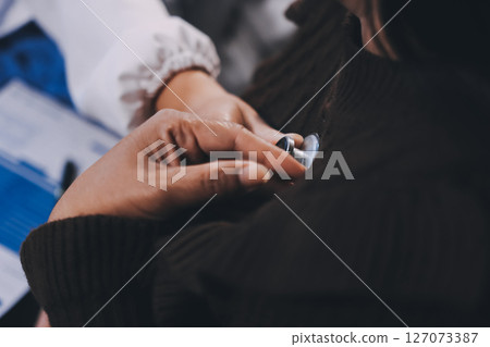 Homecare nursing service and elderly people cardiology healthcare. Close up of young hispanic female doctor nurse check mature caucasian man patient heartbeat using stethoscope during visit 127073387
