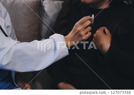 Homecare nursing service and elderly people cardiology healthcare. Close up of young hispanic female doctor nurse check mature caucasian man patient heartbeat using stethoscope during visit 127073388