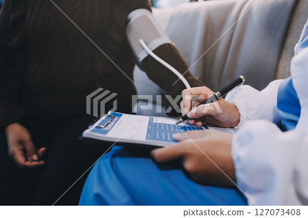 Doctor using Blood pressure monitor and stethoscope checking measuring arterial blood pressure on arm to a patient in the hospital, healthcare and medical concept 127073408