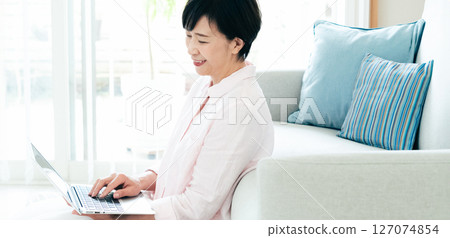 A middle-aged woman operating a computer in the living room A middle-aged woman operating a computer in the living room 127074854