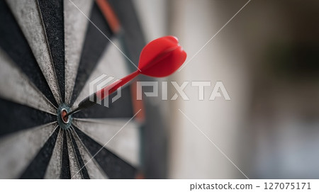 Close-up of a Red Dart Just Missing the Bullseye on a Dartboard in a Dimly Lit Environment 127075171