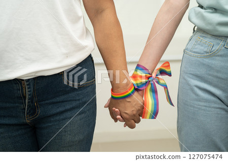 Asian LGBT couple woman holding hand wearing rainbow wristband. 127075474