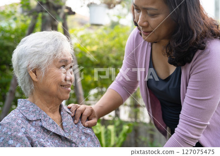Caregiver help and care Asian senior woman patient sitting on wheelchair in park. 127075475