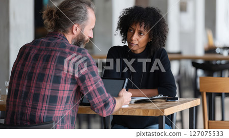 Young Mentor Demonstrating Points on Tablet During Discussion in Modern Cafe Environment 127075533