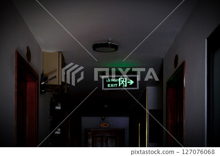 Dimly lit hallway with an illuminated exit sign 127076068