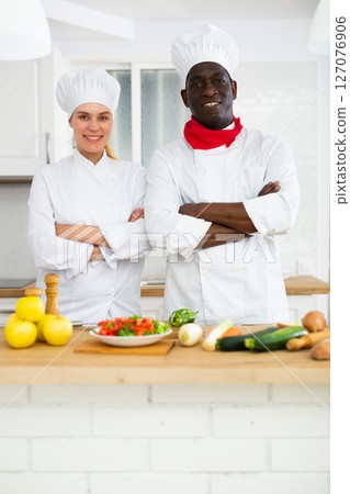 Two smiling confident personal chefs in white uniforms standing in private kitchen 127076906