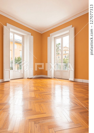 Bright and spacious room with orange walls, wooden floor, and large windows in a sunny setting Bright and spacious room with orange walls, wooden floor, and large windows in a sunny setting 127077313