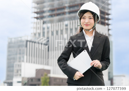 A young woman wearing a suit and helmet and holding a tablet, construction manager, site supervisor, female civil engineer A young woman wearing a suit and helmet and holding a tablet, construction manager, site supervisor, female civil engineer 127077399