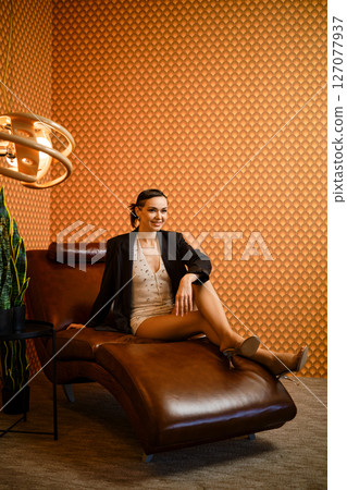 Cheerful woman sits elegantly on brown leather chaise lounge in modern interior 127077937