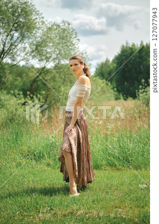 Model poses gracefully in a flowing skirt among green grass and trees on a sunny day Model poses gracefully in a flowing skirt among green grass and trees on a sunny day 127077943