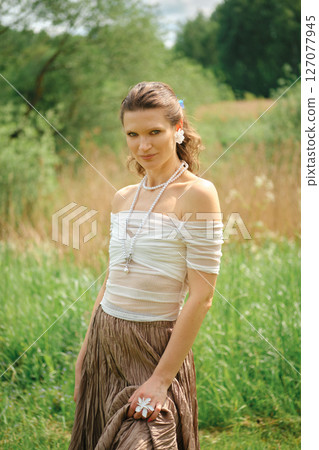 Woman in nature wearing elegant outfit stands confidently in a lush green field Woman in nature wearing elegant outfit stands confidently in a lush green field 127077945