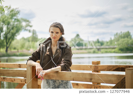 Woman in a stylish outfit poses by a serene lake during a sunny afternoon Woman in a stylish outfit poses by a serene lake during a sunny afternoon 127077946