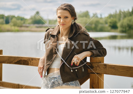 Model poses by a serene water body wearing stylish attire with a modern twist during daytime Model poses by a serene water body wearing stylish attire with a modern twist during daytime 127077947