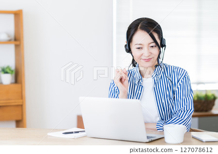 一個在客廳進行在線英語對話的中年婦女。 一個在客廳進行在線英語對話的中年婦女。 127078612