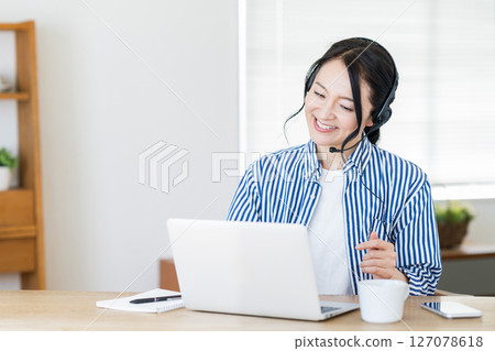 A middle-aged woman who has online English conversation in the living room. 127078618
