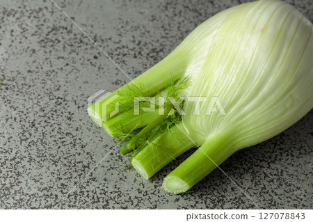 Fennel bulb with green stalks and fronds on a gray stone table. 127078843