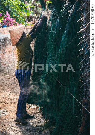 Vietnamese woman in traditional straw hat dries dyed reeds at a woven mat factory in village in Vietnam 127079076