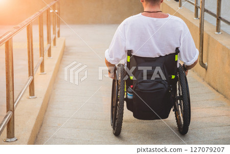 Disabled man in a wheelchair moves on a ramp to the beach. Disabled man in a wheelchair moves on a ramp to the beach. 127079207