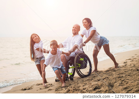 Disabled man in a wheelchair with his family on the beach. Disabled man in a wheelchair with his family on the beach. 127079314