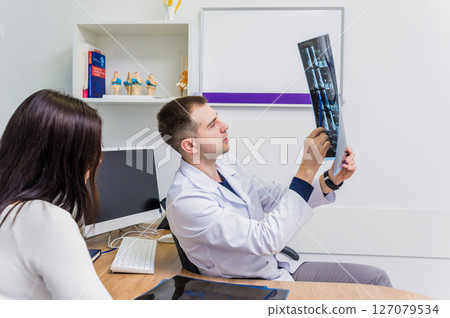 Traumatologist showing MRI film to patient in hospital. Traumatologist showing MRI film to patient in hospital. 127079534