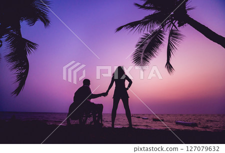 Disabled man in a wheelchair with his wife on the beach. Silhouettes at sunset Disabled man in a wheelchair with his wife on the beach. Silhouettes at sunset 127079632