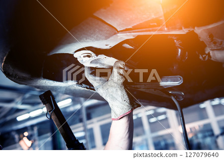 Car mechanic examining car suspension of lifted automobile at service station Car mechanic examining car suspension of lifted automobile at service station 127079640