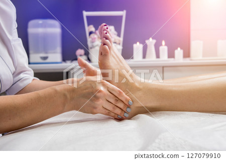 Beautiful young woman enjoying foot massage in spa salon. Cosmetology 127079910