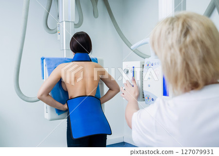 Radiologist and patient in a x-ray room. Classic ceiling-mounted x-ray system. 127079931