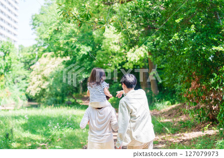 A family walking through the forest with a child on their shoulders A family walking through the forest with a child on their shoulders 127079973