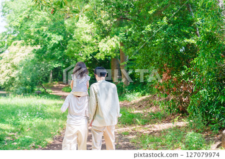 A family walking through the forest with a child on their shoulders 127079974