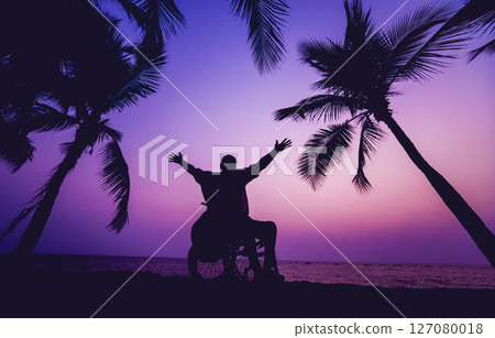 Disabled man in a wheelchair on the beach. Silhouette at sunset. 127080018