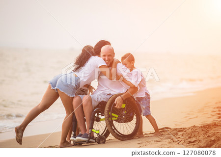 Disabled man in a wheelchair with his family on the beach. Disabled man in a wheelchair with his family on the beach. 127080078