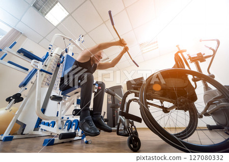 Disabled man doing strength exercises separate from the wheelchair. 127080332