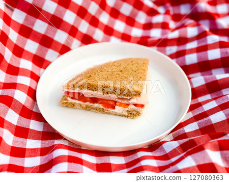 Turkey and tomato sandwich on white plate with red checkered tablecloth background 127080363
