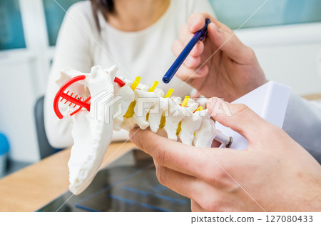 Orthopedist showing spine model to patient in hospital Orthopedist showing spine model to patient in hospital 127080433