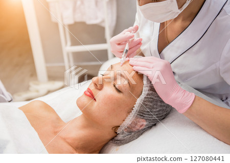 The doctor cosmetologist makes the facial injections procedure. The doctor cosmetologist makes the facial injections procedure. 127080441
