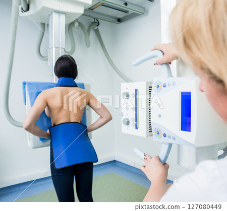 Radiologist and patient in a x-ray room. Classic ceiling-mounted x-ray system. 127080449