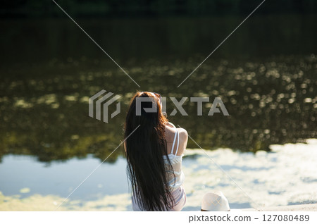 A girl sits on the shore of a lake 127080489