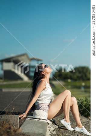 A girl wearing shorts, a T-shirt and sunglasses is sitting on warm soil. A girl wearing shorts, a T-shirt and sunglasses is sitting on warm soil. 127080492