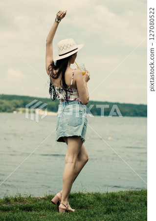 The girl is standing with her face turned to the lake and her back to the camera 127080522