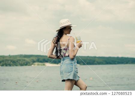 A young girl stands by the lake with a bright cup of juice in her hand 127080523