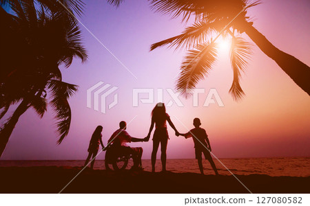 Disabled man in a wheelchair with his family on the beach. Silhouettes at sunset 127080582