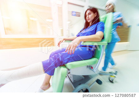 Nurse moves mobile medical chair with patient at hospital. Medical equipment. 127080587