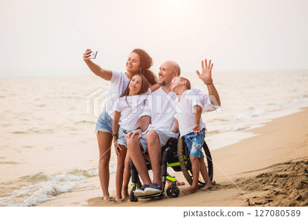 Disabled man in a wheelchair with his family on the beach. 127080589