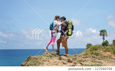 A young couple are hiking on a rugged rocky cliff that offers a view of the ocean A young couple are hiking on a rugged rocky cliff that offers a view of the ocean 127080706