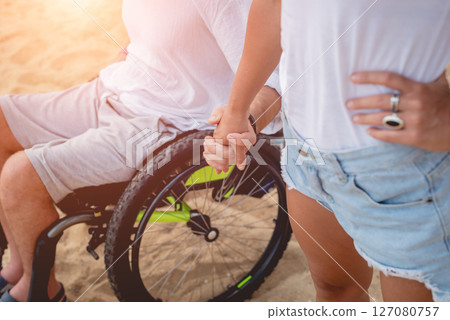 Disabled man in a wheelchair with his wife on the beach. Disabled man in a wheelchair with his wife on the beach. 127080757