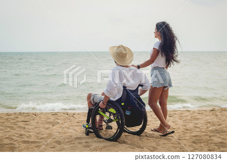 Disabled man in a wheelchair with his wife on the beach. Disabled man in a wheelchair with his wife on the beach. 127080834