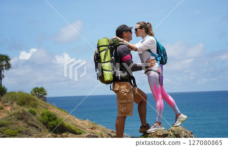 A young couple are hiking on a rugged rocky cliff that offers a view of the ocean 127080865