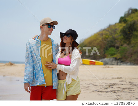 A young couple are leisurely walking along the beach, holding hands and enjoying the warm sun 127080870