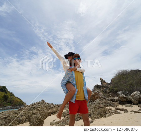 A young couple are leisurely walking along the beach, holding hands and enjoying the warm sun 127080876
